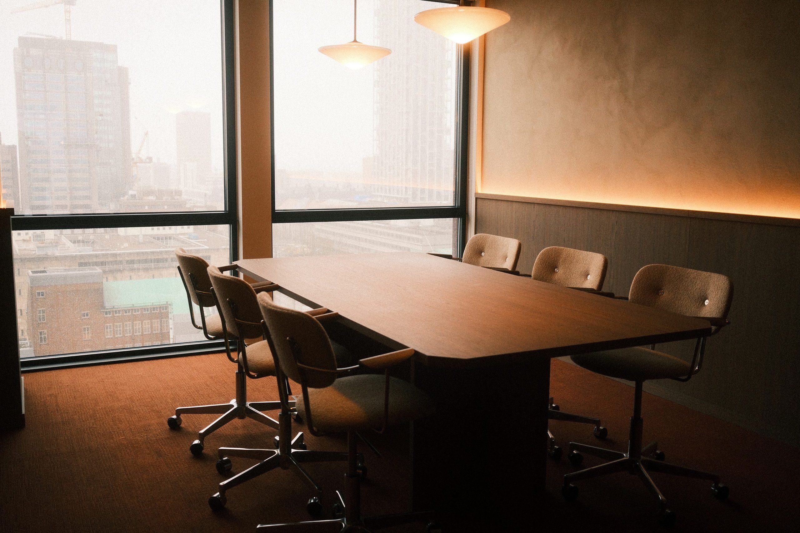 Meeting room with a long timber table and chairs in front of tall windows overlooking Rotterdam, with two pendants and a line of light above the wall panelling