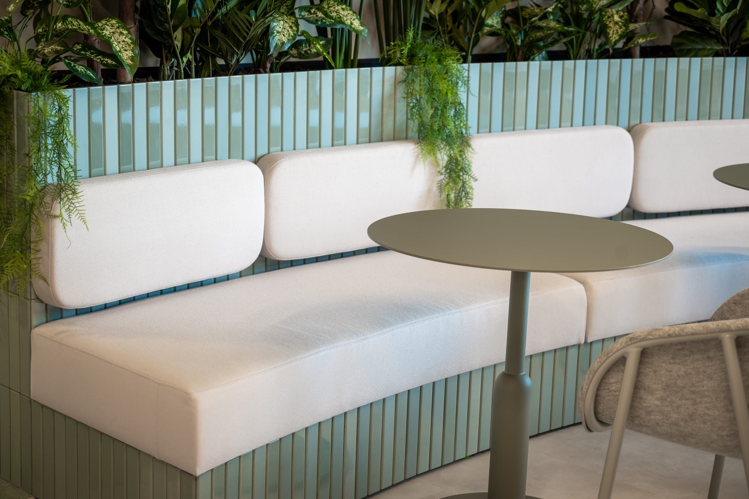 Curved banquette with white cushions, green tiled base and a round table