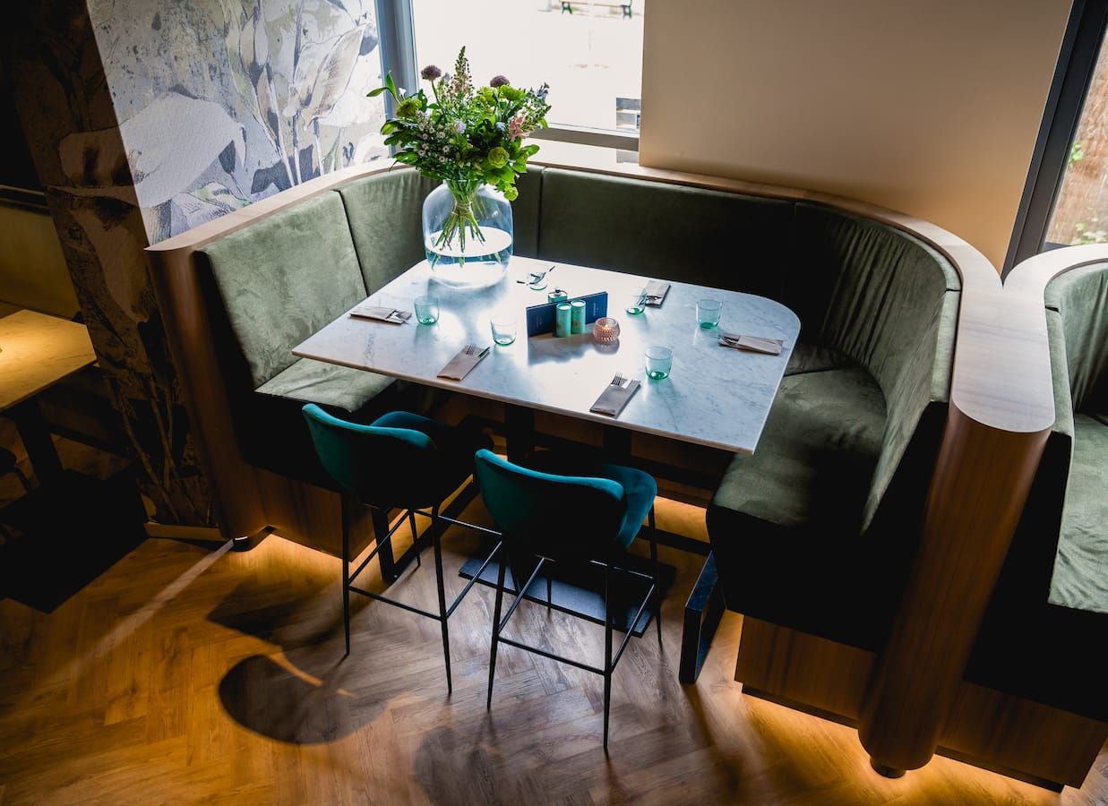 Corner booth with green velvet seating and marble table by the window at Finca