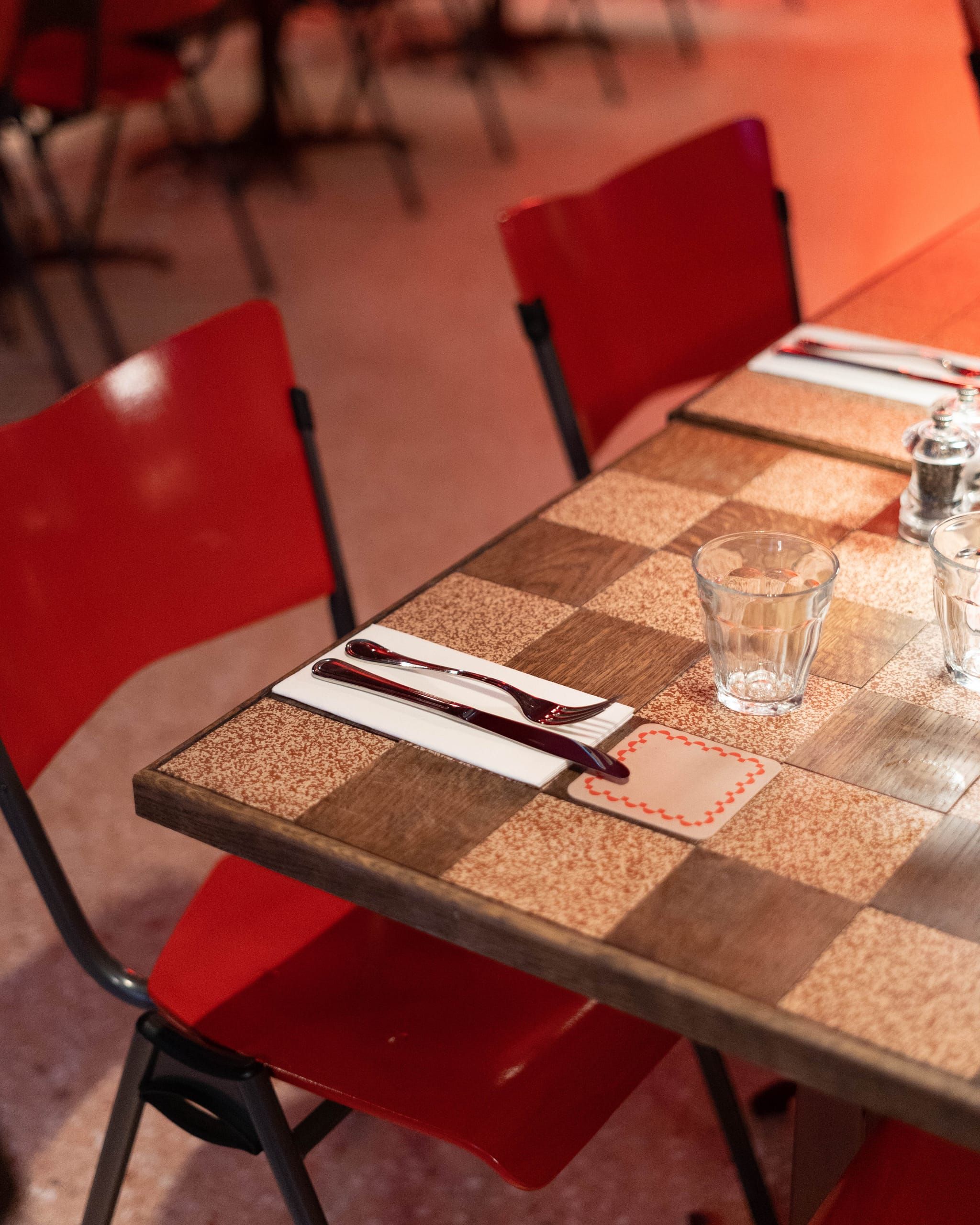 Checkerboard terrazzo and wood table top with red chairs at Mamarazzi