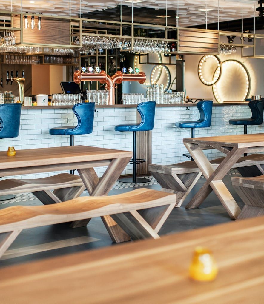 Wooden benches and tables in front of the bar with blue leather stools