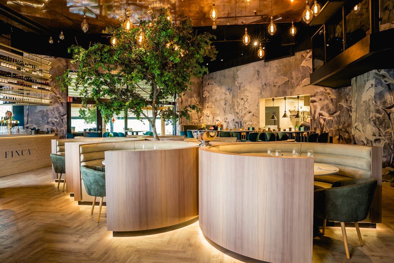 Curved wooden booths, indoor tree and pendant lights above a herringbone floor