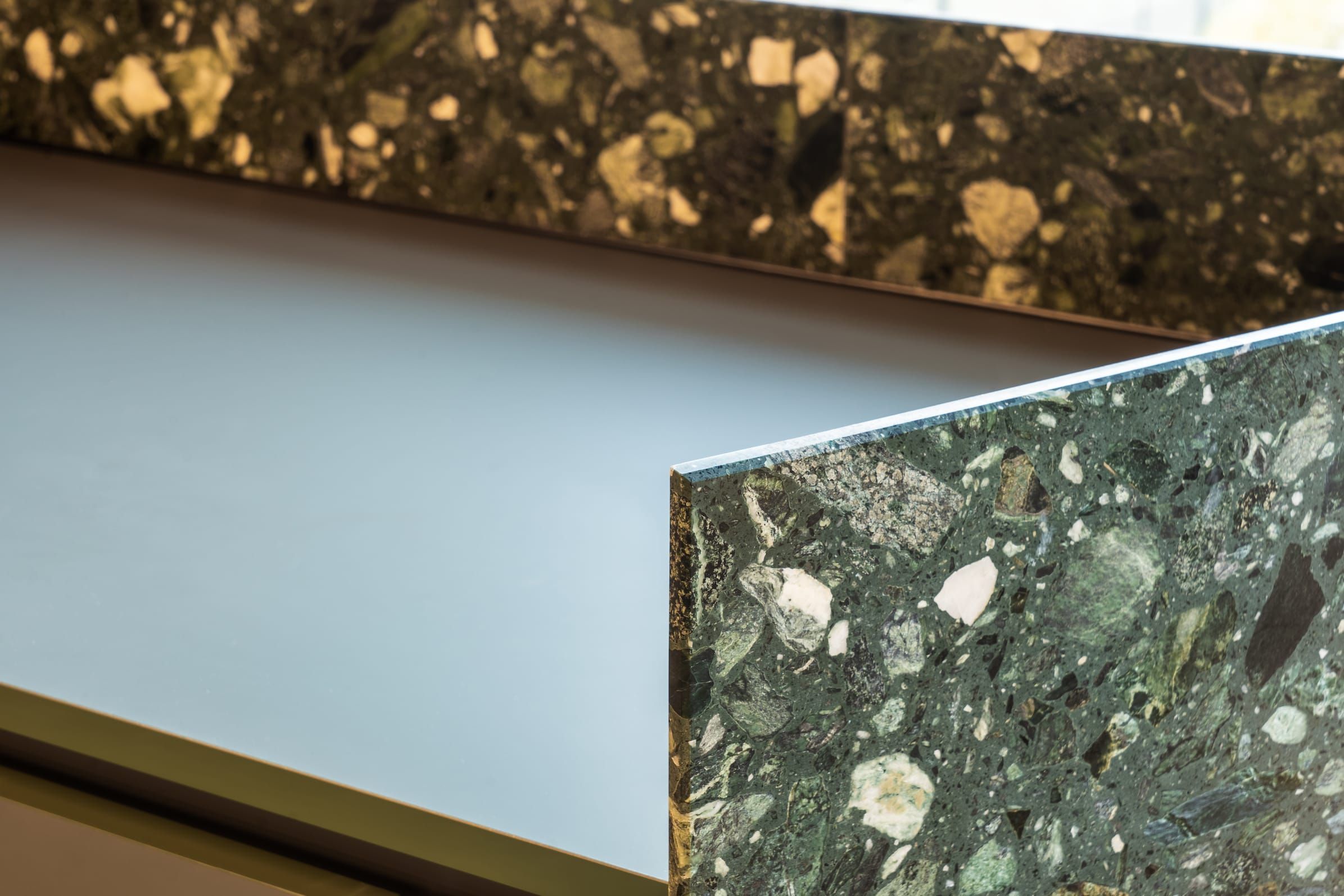 Close-up of green terrazzo counter edges with a smooth pale worktop