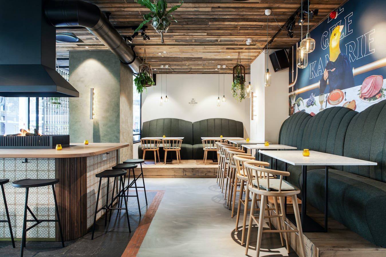 Open fire grill, tiled counter and green banquette with a mural at De Gele Kanarie