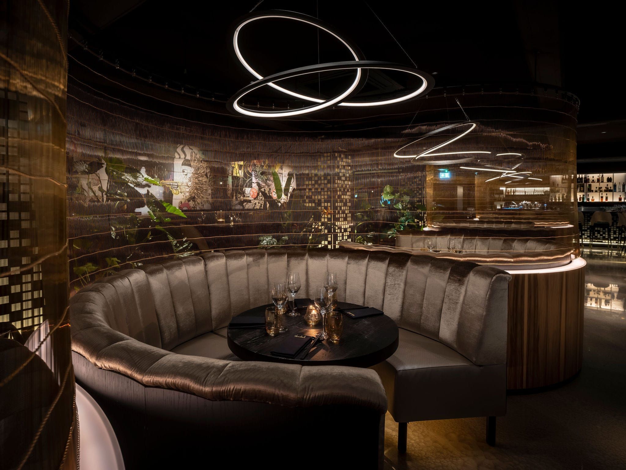 Round velvet booth beneath ring pendant lights in a dark dining room at Vandal