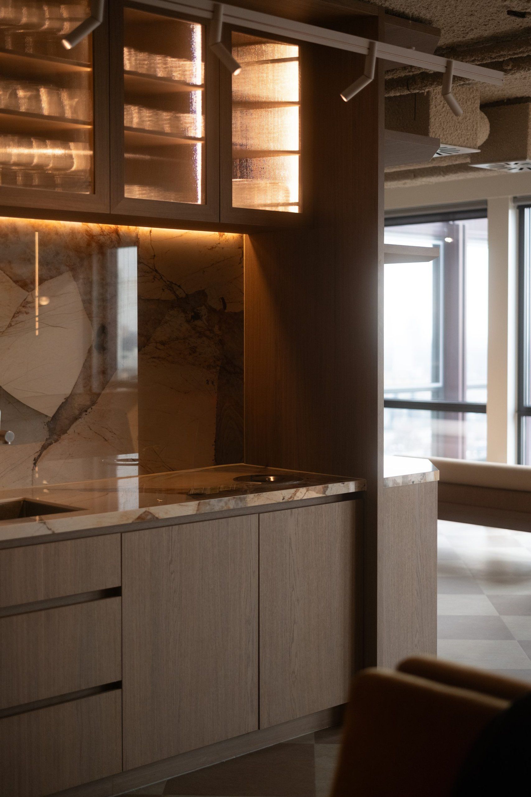 Pantry with a marble splashback, lit glass upper cabinets and spotlights on a track