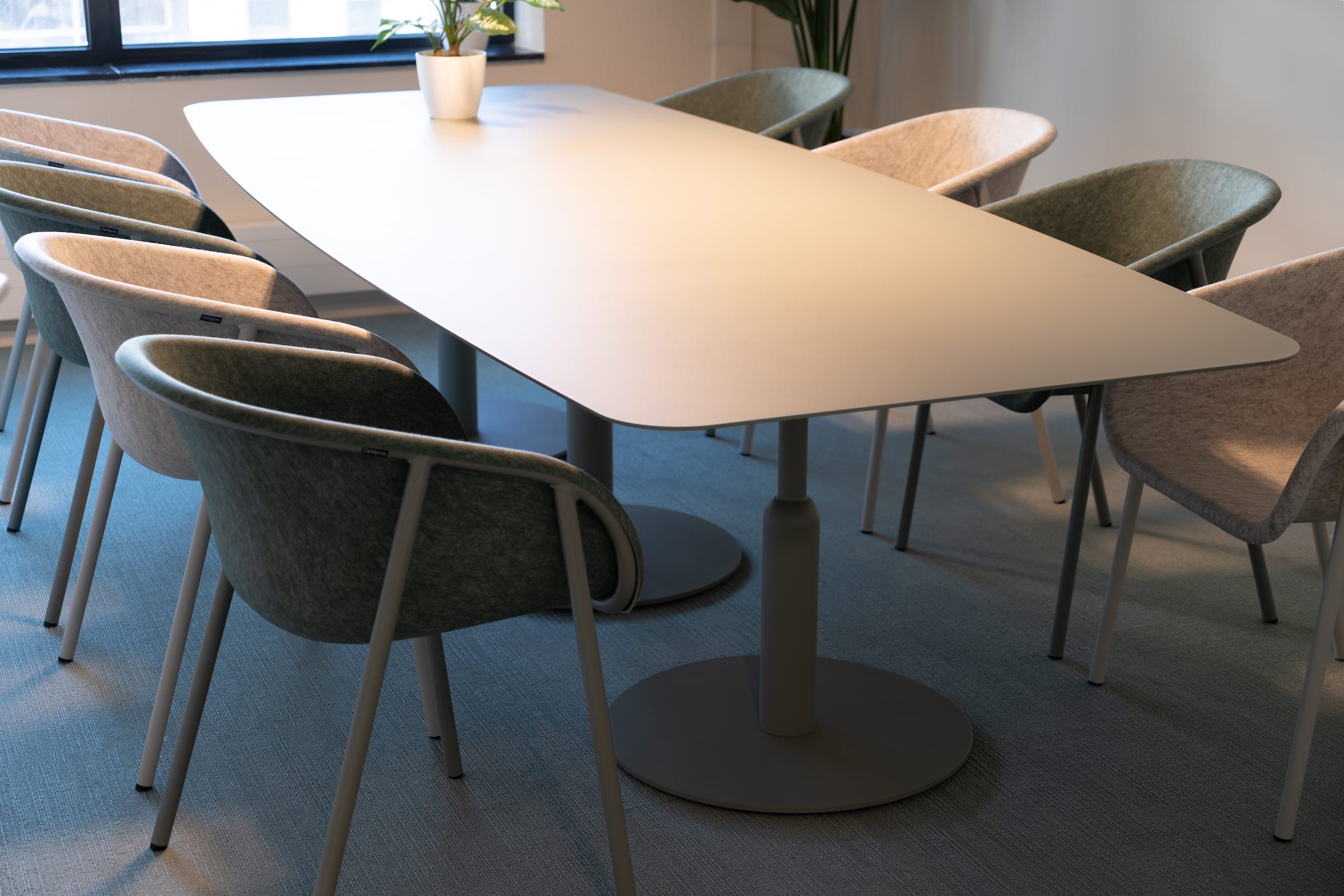 Meeting table with felt armchairs in green and pink on blue-grey carpet
