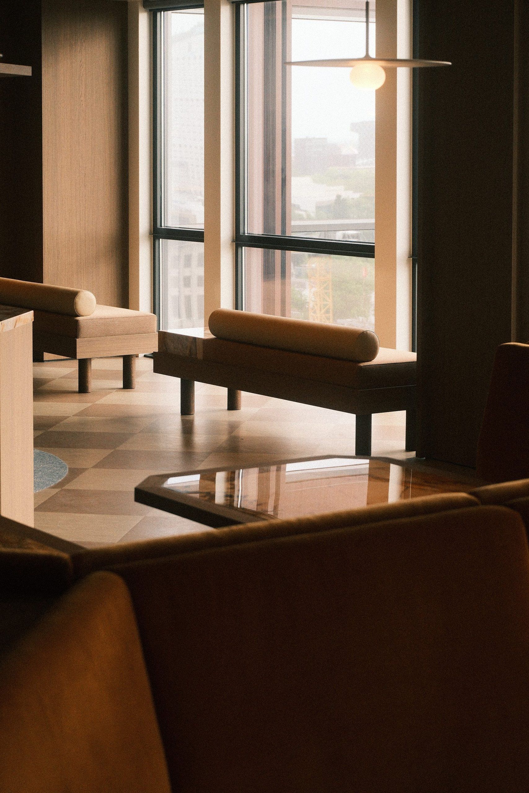 Lounge corner with low sofas by a window, beneath a flat pendant