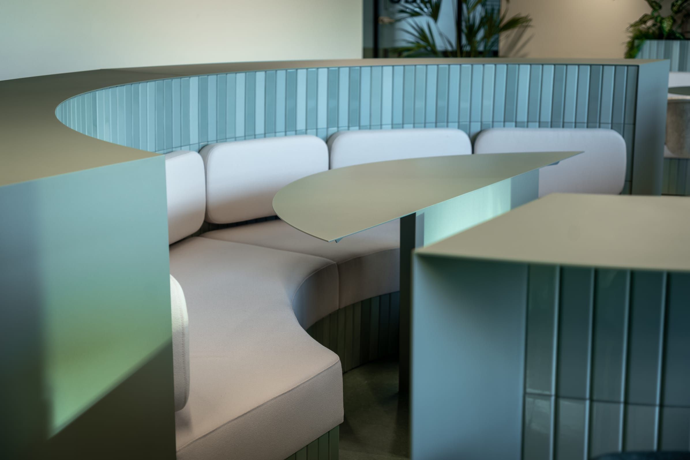 Curved green tiled seating booth with white cushions and a sculptural tabletop