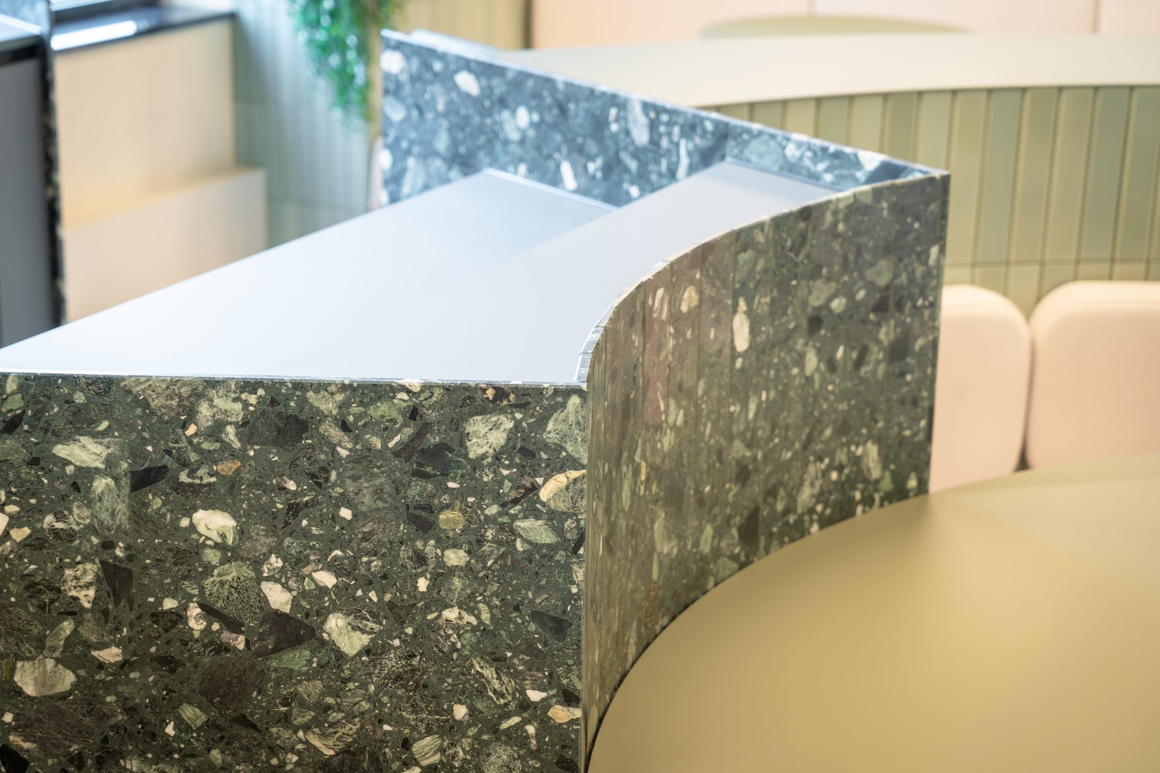 Curved green terrazzo counter edge above round tabletops and cushions