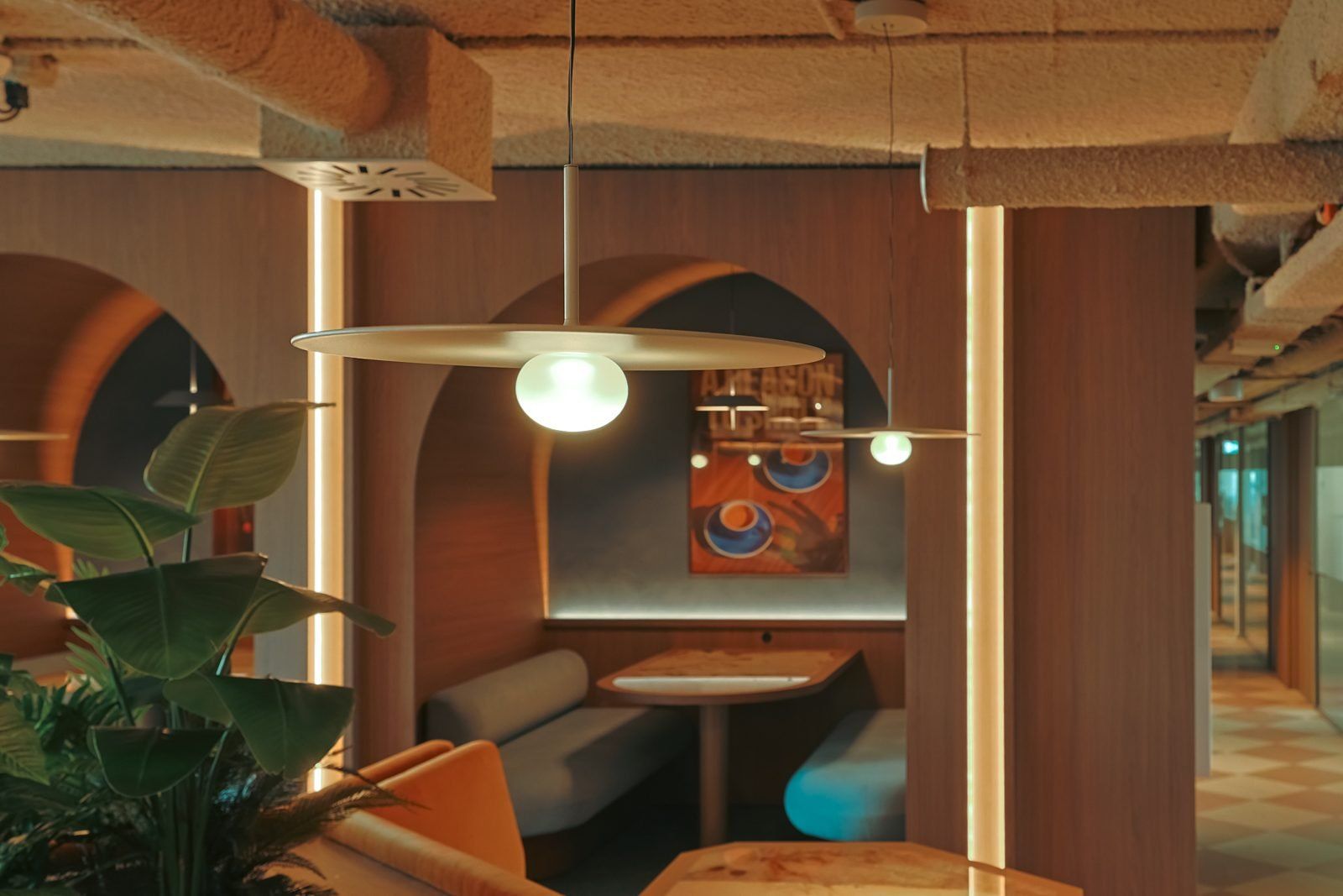 Seating niche in an arch with a glass pendant above the table, lit lines along the timber columns and plants in the foreground