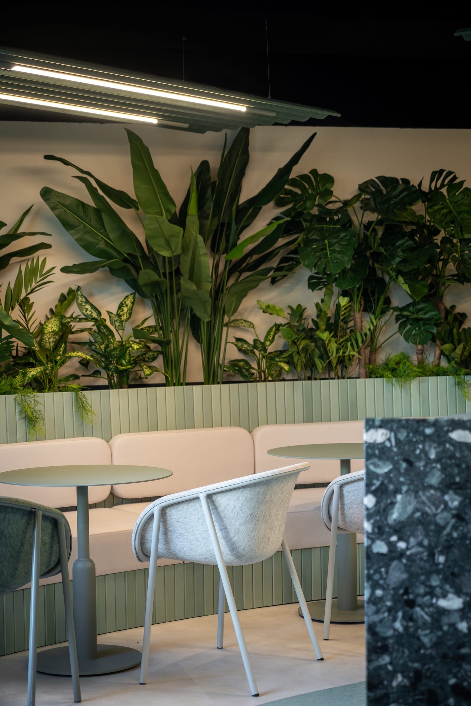 Lush plants above a green tiled banquette with a felt chair and terrazzo wall