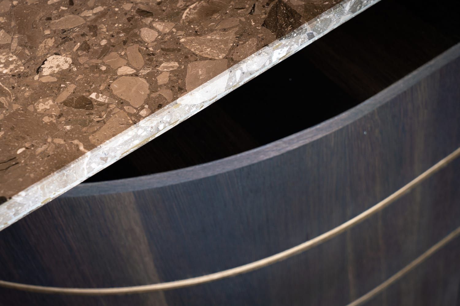 Close-up of a terrazzo counter edge above a curved dark oak panel with brass inlay