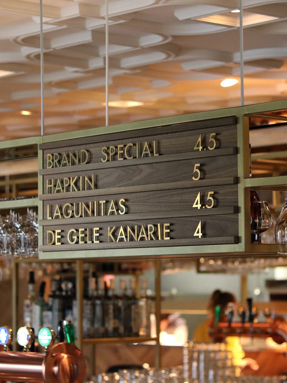 Wooden beer menu board with brass lettering above the bar