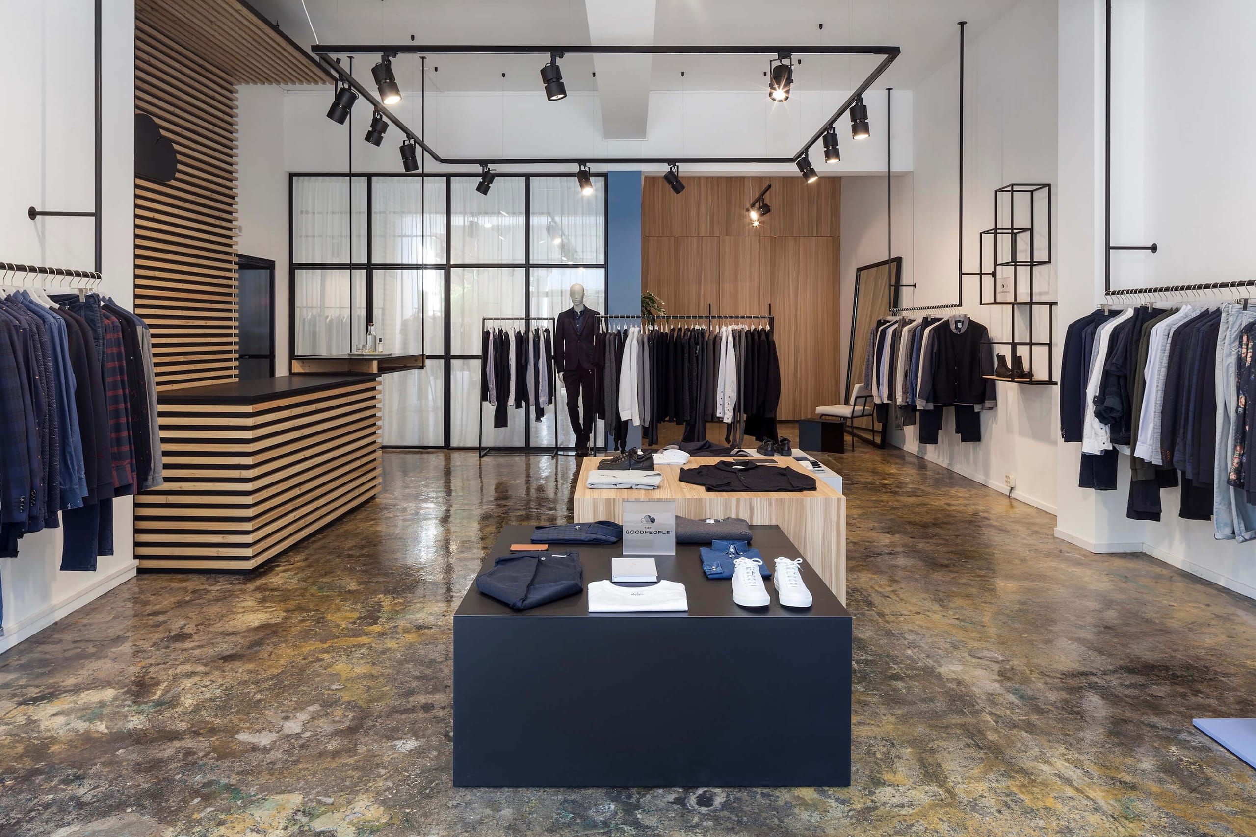 Fashion store with clothing rails, oak and black display tables and a polished concrete floor